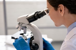 Concentrated laboratory worker in gloves using microscope while analyzing cell structure