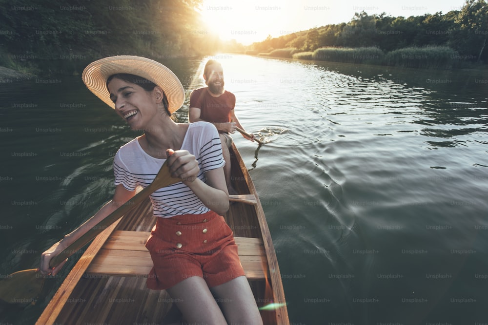 Paar genießt das Paddeln mit dem Kanu auf dem Sonnenuntergangssee. Frau und Mann auf einer gemütlichen Bootsfahrt.