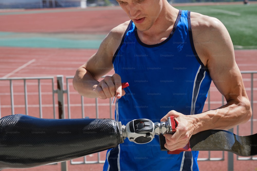 Primer plano de un hombre arreglando una pierna artificial con un destornillador en el estadio en un día soleado