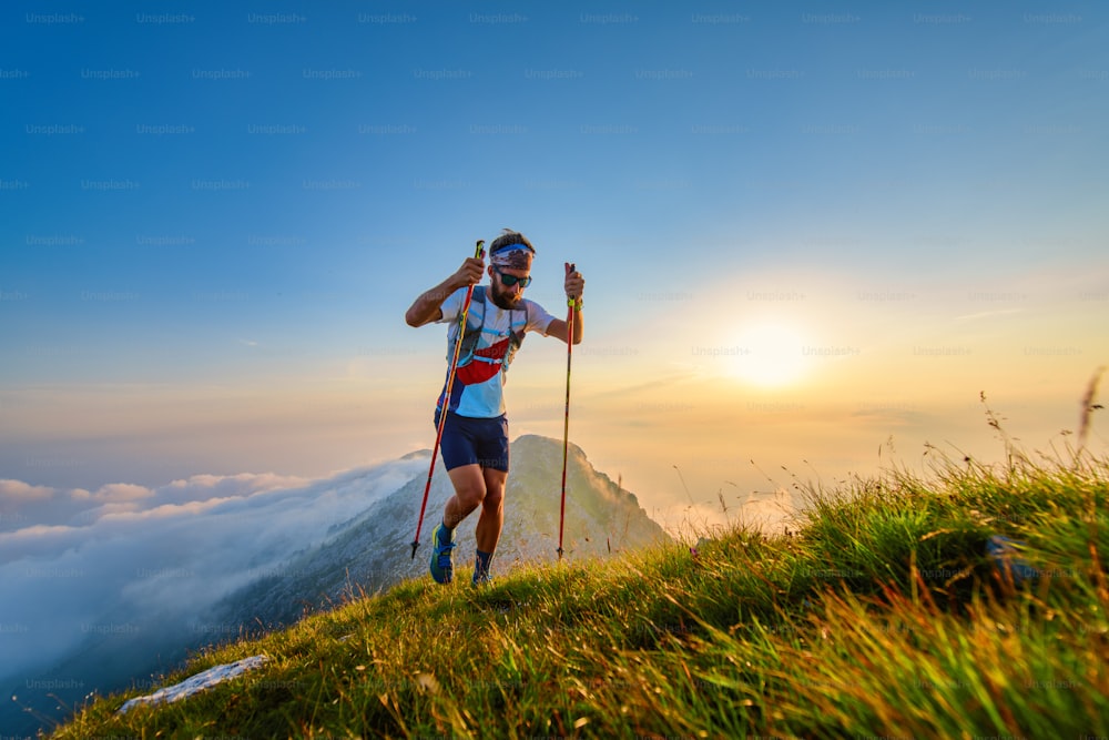 Hombre con postes en las montañas con puesta de sol detrás