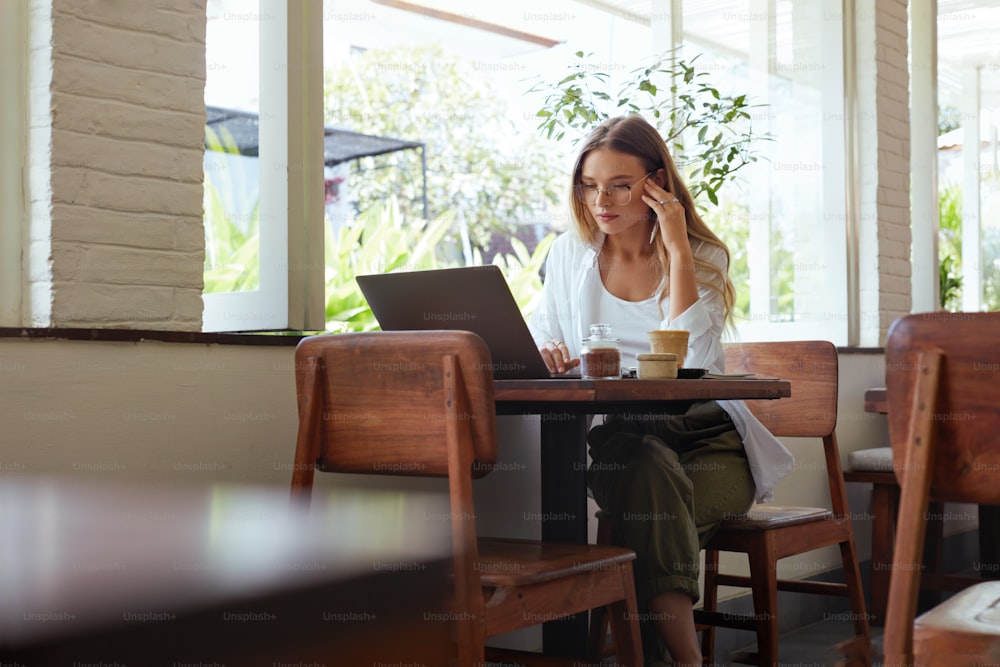 Woman. Online Work At Cafe. Beautiful Girl In Casual Clothes Working On Laptop And Touching Head. Modern Digital Technologies For Remote Job Or Education At Comfortable Workplace.