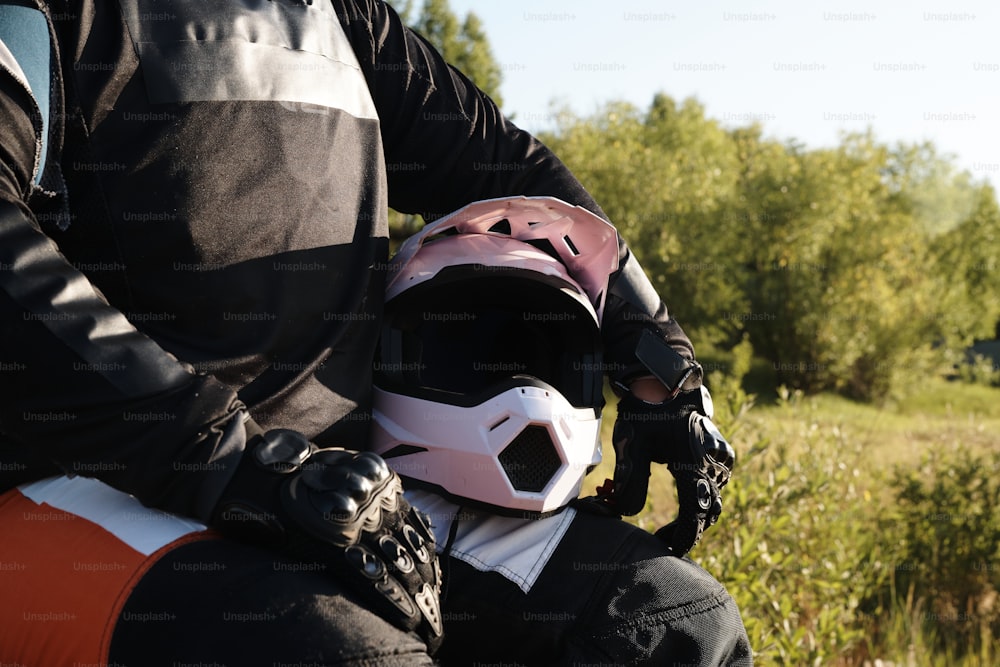 Nahaufnahme eines nicht erkennbaren Motorradfahrers in Schutzhandschuhen, der mit Helm im Wald sitzt