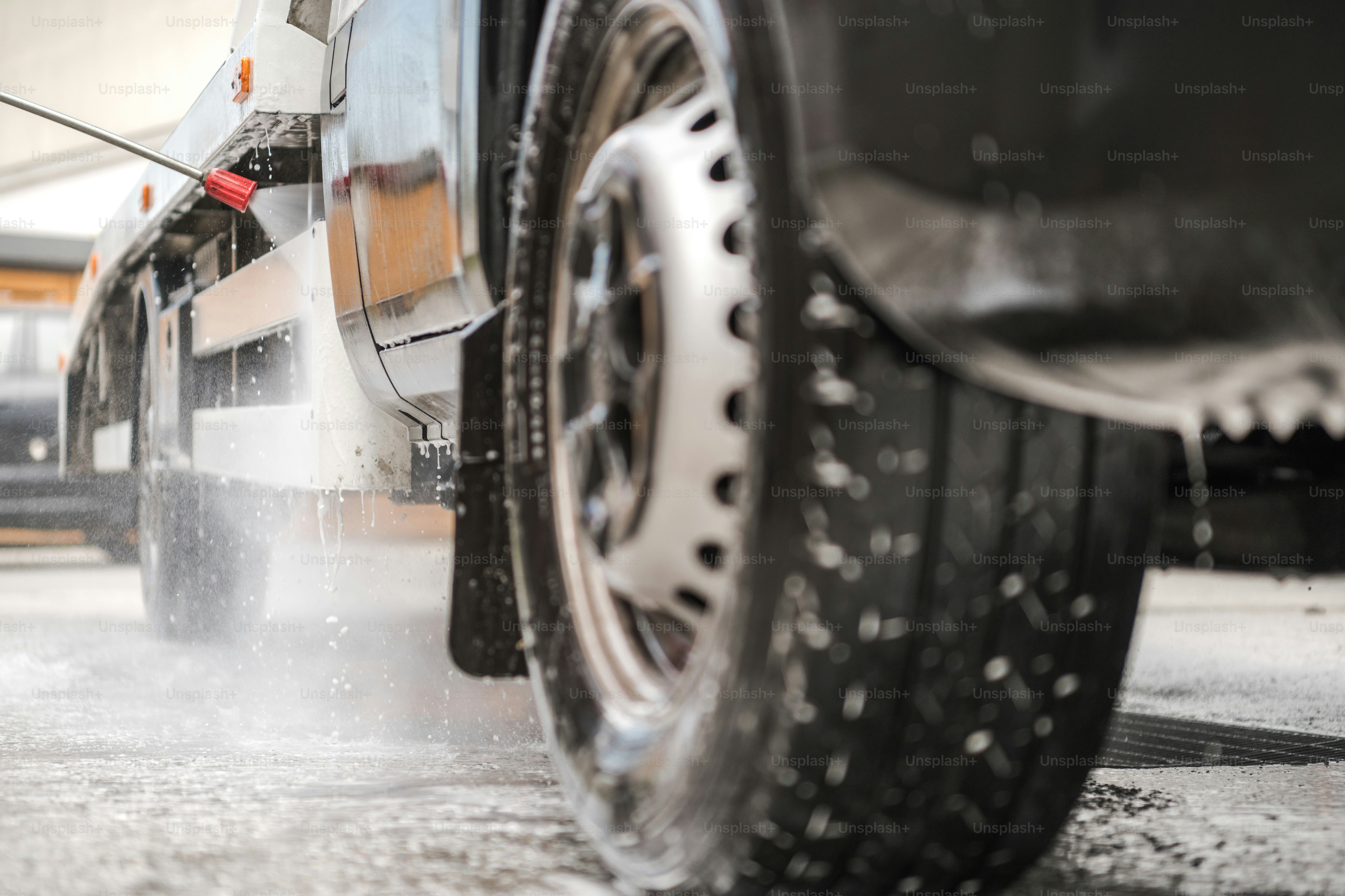 Image Of Person Pressure Washing Commercial Truck With Hose And Wand Inside Of Car Wash.