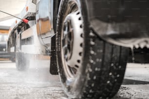 Image d’une personne lavant à pression un camion commercial avec un tuyau et une baguette à l’intérieur d’un lave-auto.