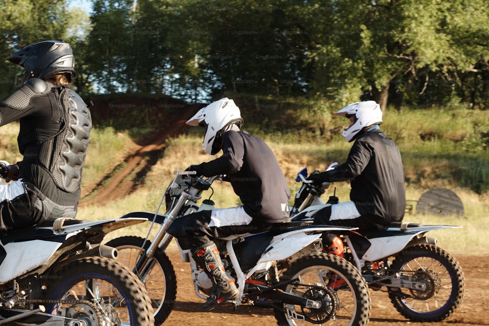 Group of sporty men in helmets enjoying motorcycle racing at off-road track in forest