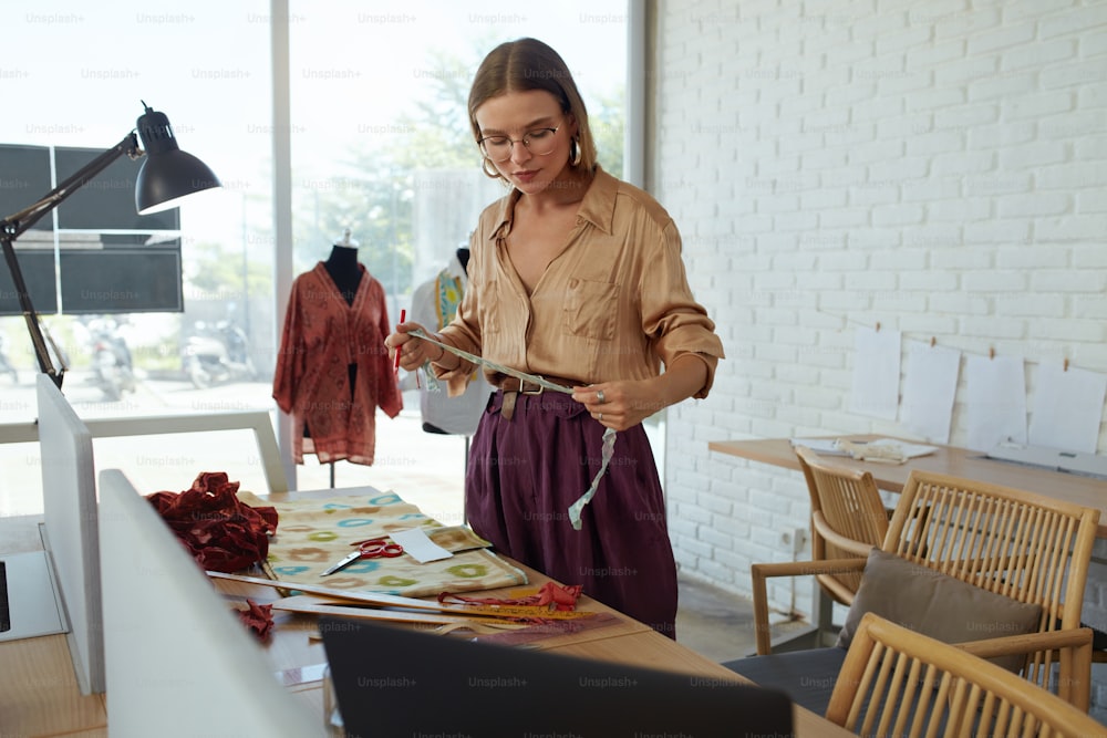 Arbeit. Modedesigner bei Workshop. Schöner Schneider Maßstoff für neues Kleid. Erfolg Selbstständige Frau in stilvoller Kleidung arbeitet im Atelier. Professionelle Schneiderin im eigenen Studio.