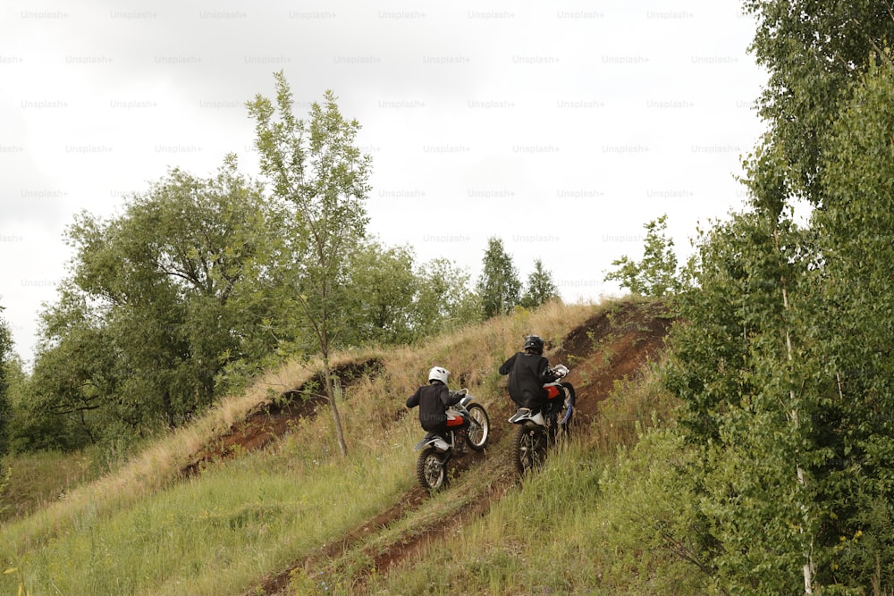 Vista traseira de motociclistas extremos em capacetes atingindo a velocidade enquanto sobem a colina em estrada acidentada
