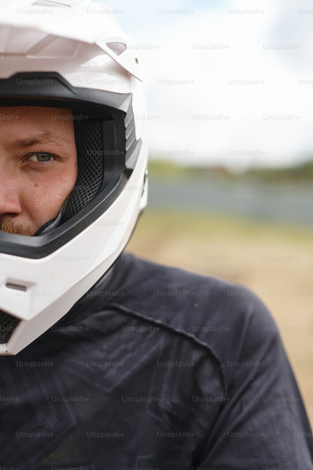 屋外に立つヘルメットとジャケットを着た深刻な残忍なモーターサイクリストの肖像画