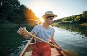 Couple enjoy paddling canoe on the sunset lake. Woman and man on a leisurely boat ride.