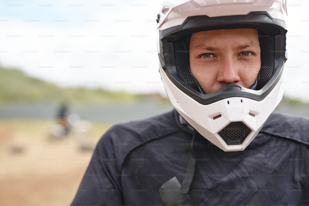 Ritratto di giovane motociclista maschio serio in casco bianco in pista fuoristrada