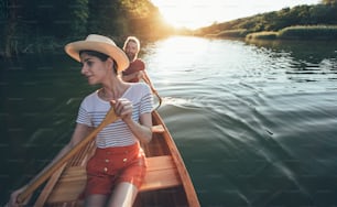 Couple enjoy paddling canoe on the sunset lake. Woman and man on a leisurely boat ride.