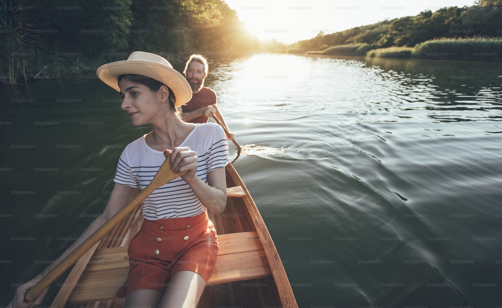 La coppia si diverte a pagaiare in canoa sul lago al tramonto. Donna e uomo su un piacevole giro in barca.
