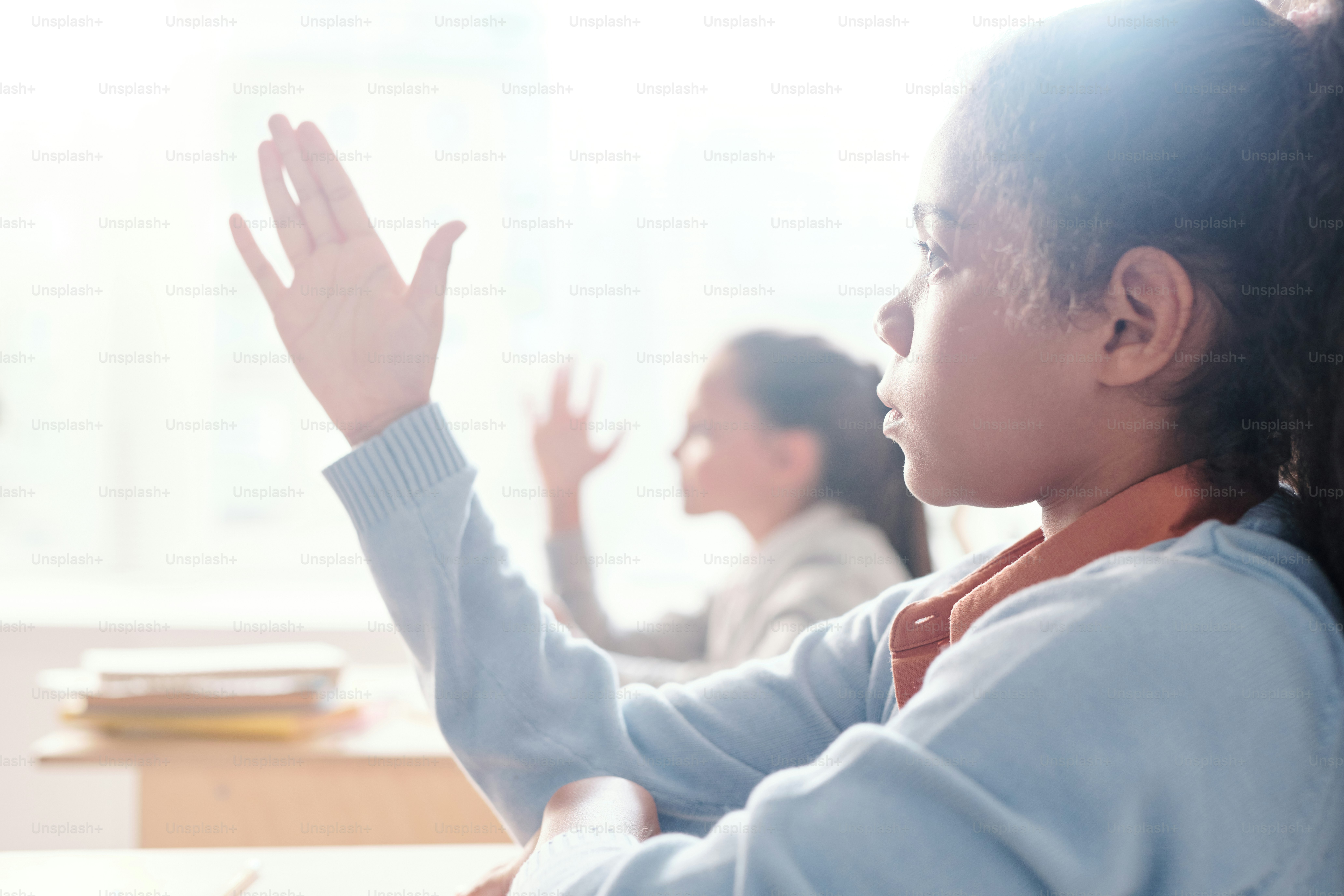 Clever cute schoolgirls willing to answer or ask questions after listening to explanation of teacher while sitting by desks in classroom