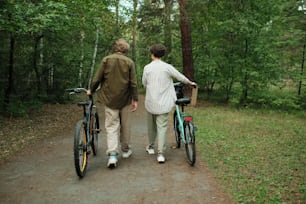 캐주얼 웨어를 입은 젊은 커플이 숲길이나 푸른 나무 사이의 길을 따라 이동하는 동안 서로 이야기하는 뒷모습