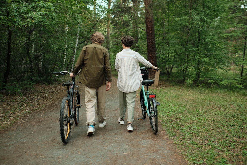 Vista posteriore di una giovane coppia in abbigliamento casual che parla tra loro mentre si muove lungo il sentiero della foresta o la strada tra gli alberi verdi