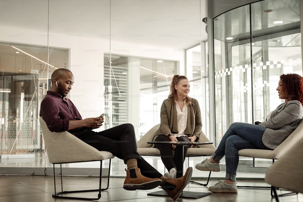 Drei unterschiedliche Geschäftsleute hängen während ihrer Pause zusammen im Loungebereich eines modernen Büros ab