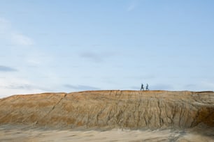 Tiny silhouettes of two contemporary researchers in protective coveralls moving on top of long hill against clear blue sky