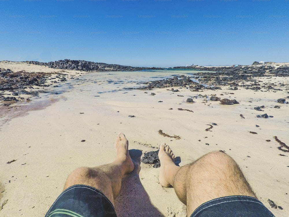 Alternative point of view of man legs at the beach with swimwear enjoying the sand and the blue water and sky in summer holiday vacation