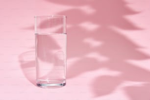 Bicchiere d'acqua e ombra foglia su sfondo rosa