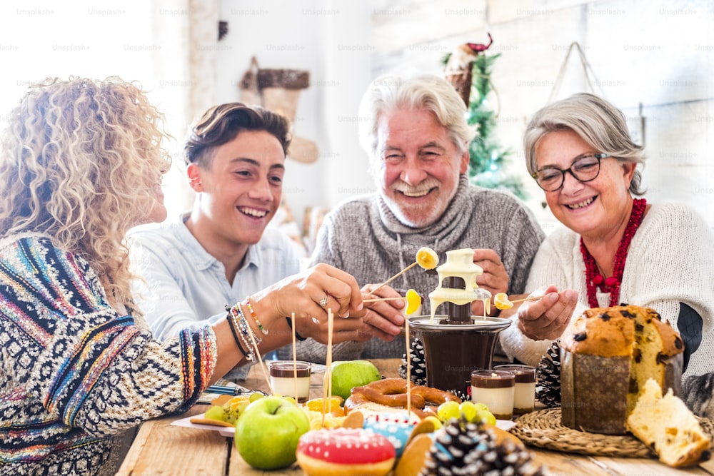 世代が混在する陽気な家族は、チョコレートとケーキと無料で自宅でクリスマスの冬のイブランチを一緒に楽しみます-人々は友情と愛でイベントを祝います-白い家の屋内と木製のテーブル