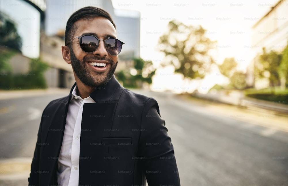 Smiling bearded Indian arabic business man standing confidently with his arms crossed looking into the distance wearing sunglasses