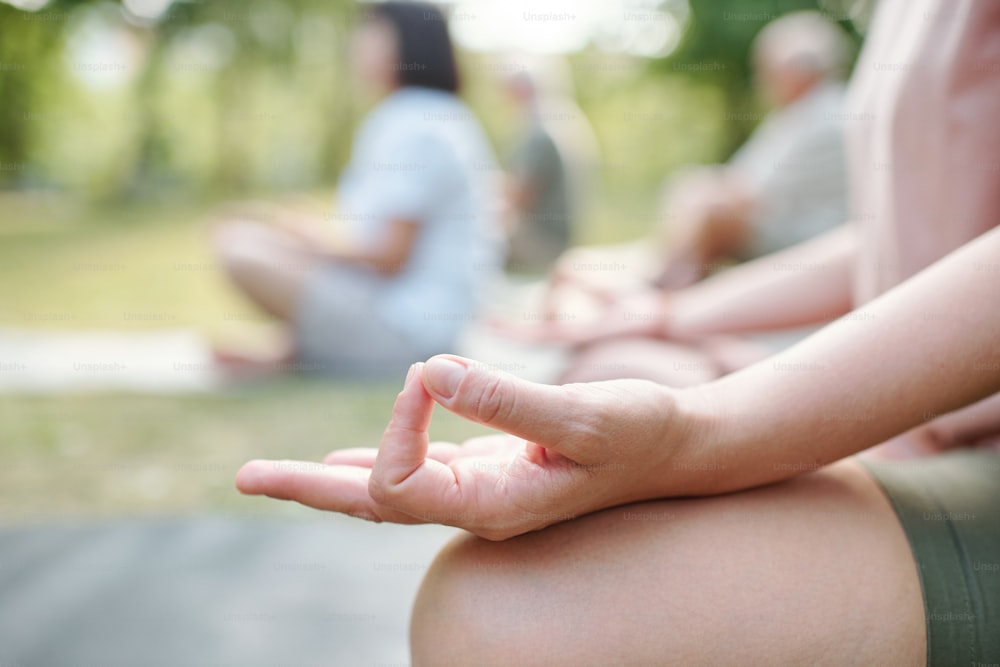 Close-up of unrecognizable woman touching fingers in mudra while meditating at group class outdoors