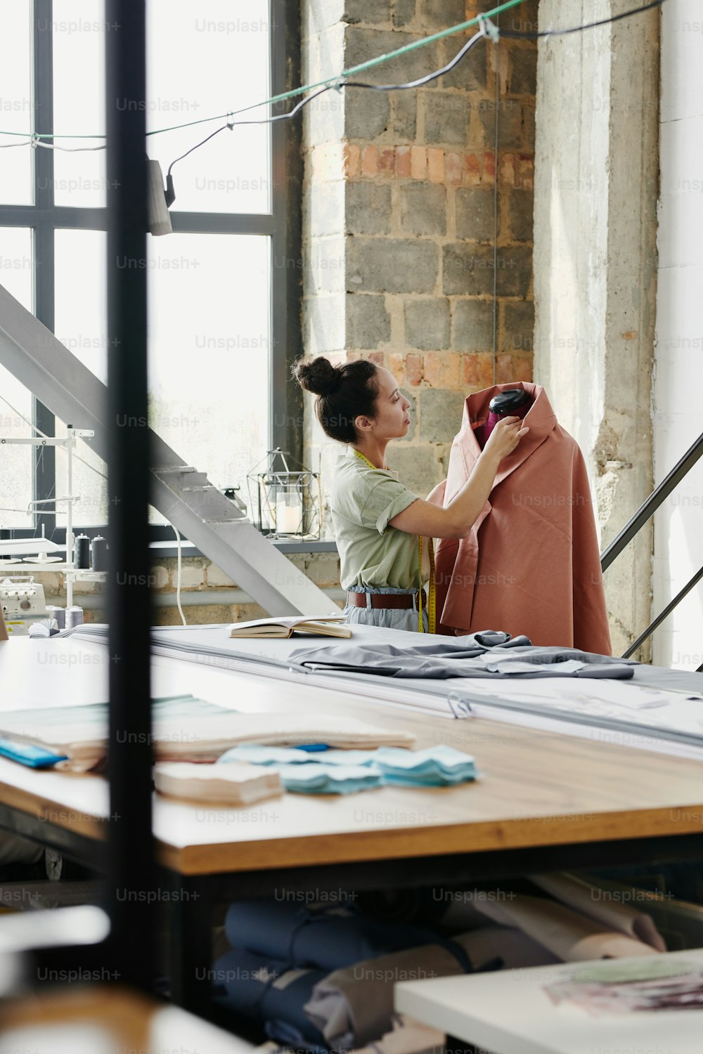 현대 패션 디자인 스튜디오의 여성 노동자는 작업장에서 새로운 계절 컬렉션을 작업하는 동안 더미에 의류 아이템을 바느질합니다.