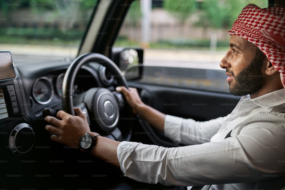 Bearded arab businessman wearing traditional Keffiyeh head scarf driving a car