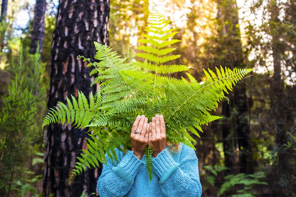 Portrait of un recognizable people hidden by big leafs from nature forest - concept of earth's day and natural outdoor environment leisure activity - no deforestation and save the planet lifestyle