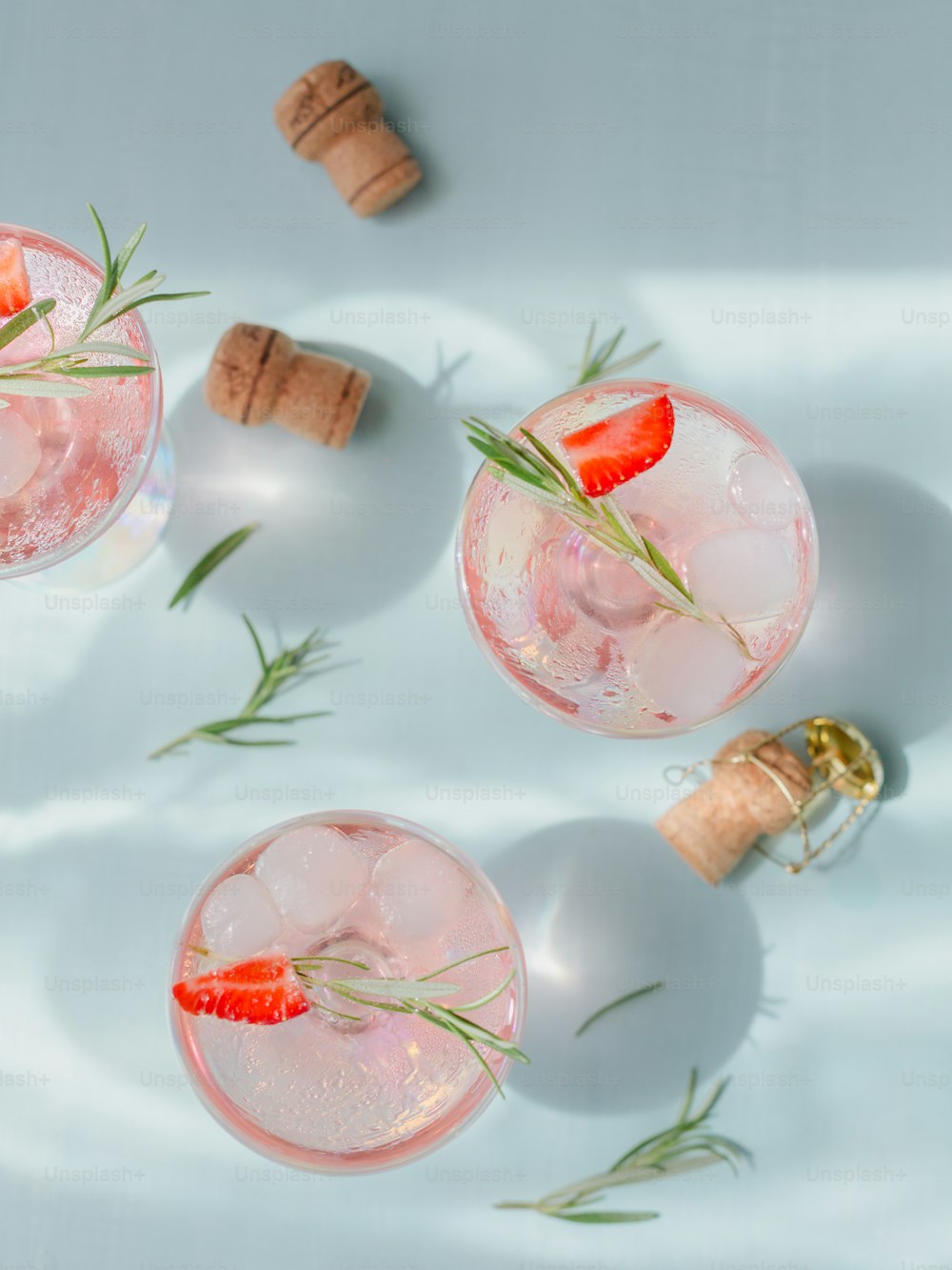Sommergetränk mit weißem Sekt. Hausgemachter erfrischender Fruchtcocktail oder Punsch mit Champagner, Erdbeeren, Eiswürfeln und Rosmarin auf hellblauem Hintergrund.