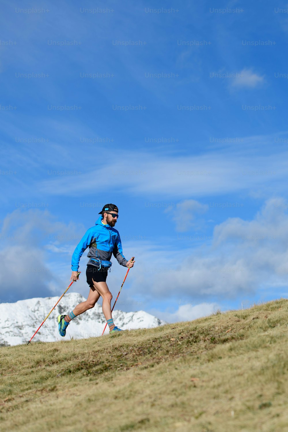 A man trains for ultra run trail on hilly meadow in autumn with the first snow on the mountains