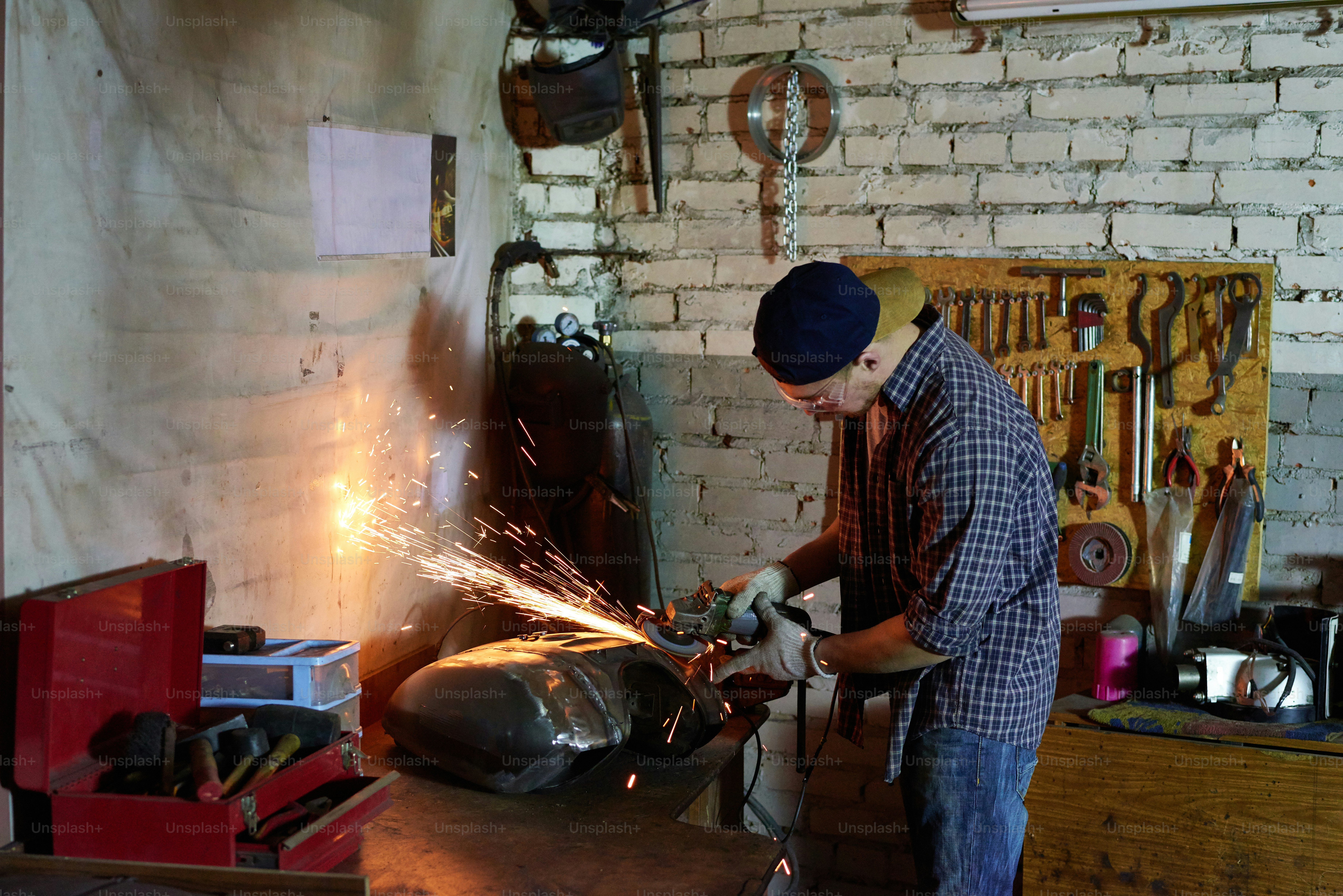 Man grinding motorbike fuel tank part in his workshop horizontal shot ...