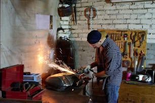 Man grinding motorbike fuel tank part in his workshop horizontal shot