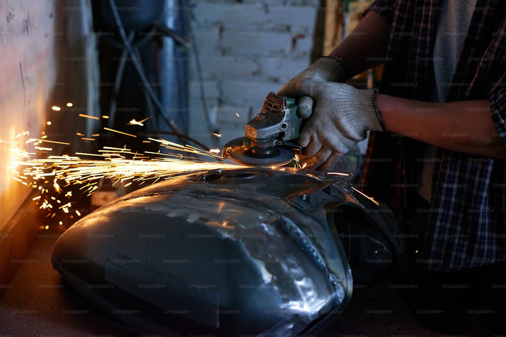 Unrecognizable repairman wearing checked shirt grinding motorbike fuel tank part