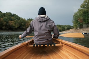 Rear view of man paddling canoe in the lake forest.