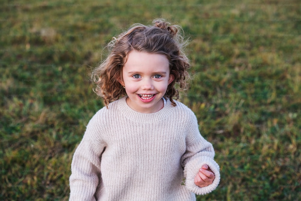 Portrait of cheerful small girl standing in autumn nature, looking at camera.