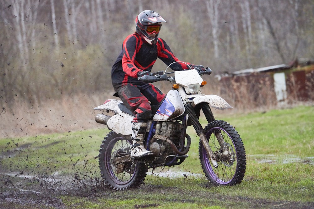 Motorcross rider racing in mud track against dry trees and green lawn