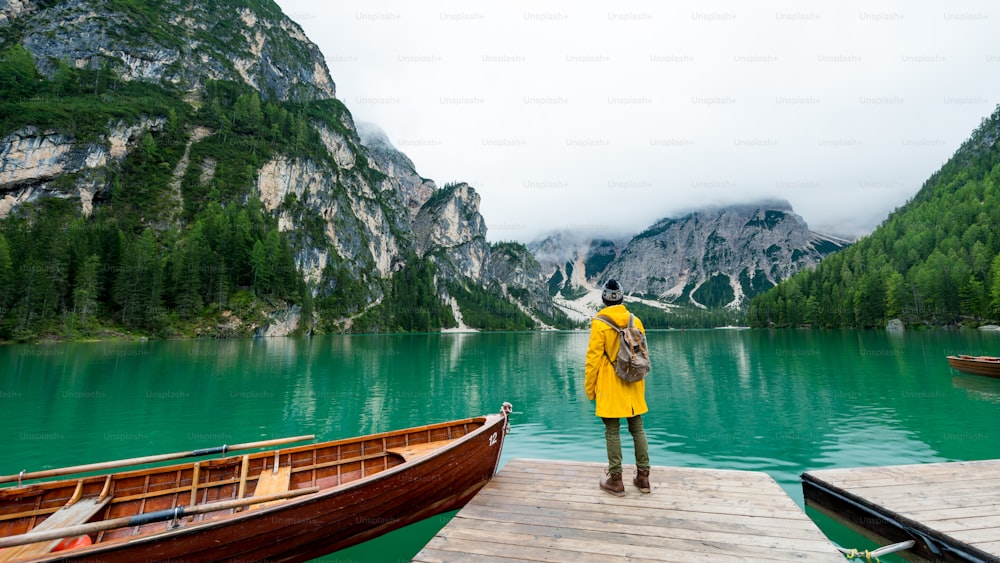 Rückansicht Porträt eines Wanderers mit ausgestreckten Armen beim Besuch des Alpensees in Prags, Italien. Glückliche Wanderer in gelber Jacke und Rucksack genießen die Naturlandschaft im Herbst. Fernweh und Reisen.
