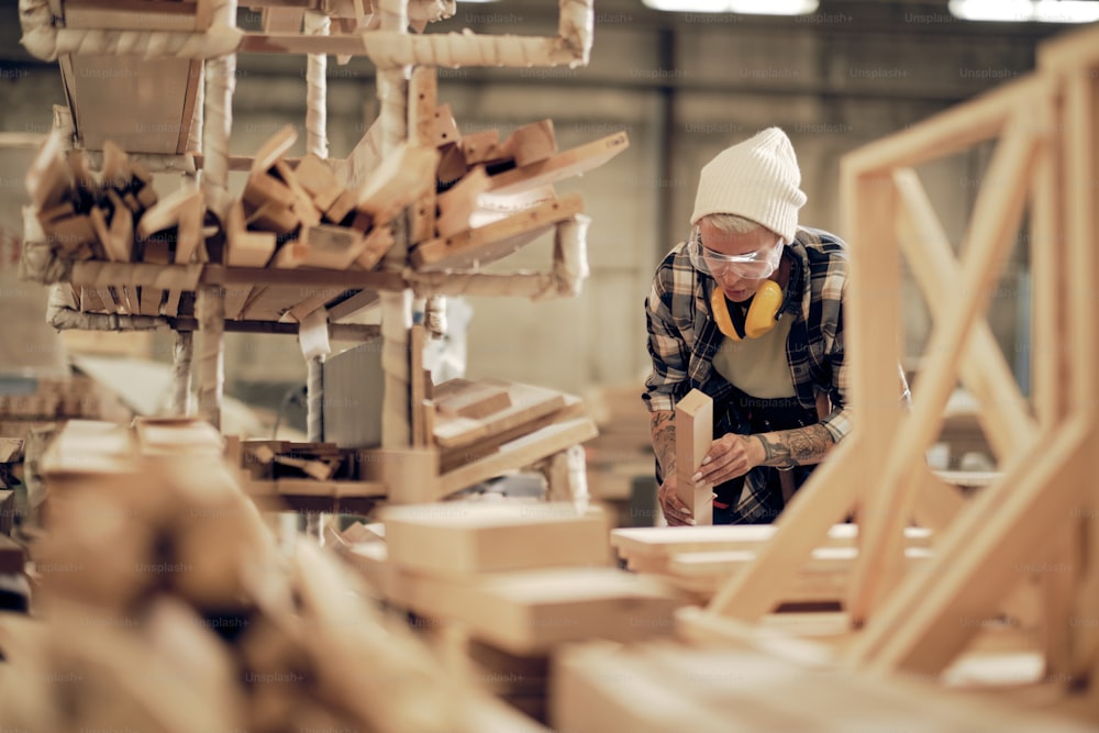 Retrato ambiental de una carpintera fuerte que trabaja con madera en la fábrica, con equipo de protección