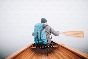 Rear view of man paddling canoe in the foggy lake.