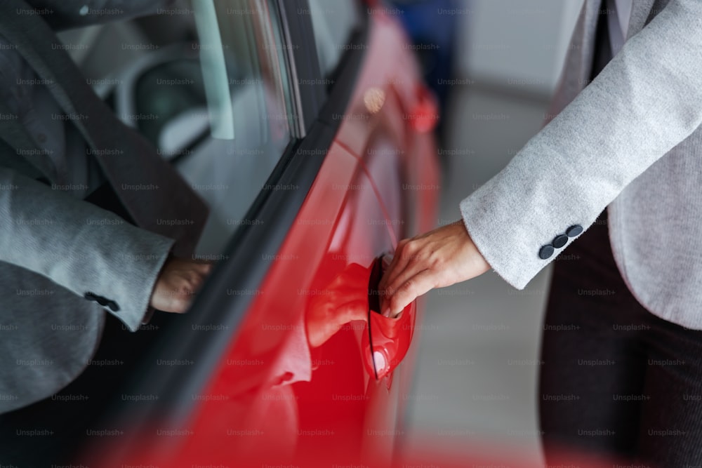 Closeup of female car seller opening car door while standing in car salon.