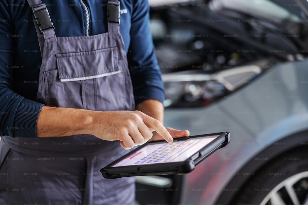 Mechanic using tablet for diagnosing a car issue. Garage of car salon interior.
