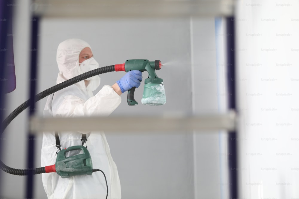 보호 복과 인공 호흡기를 입은 남자가 벽에 페인트를 뿌립니다. 페인팅 서비스 개념