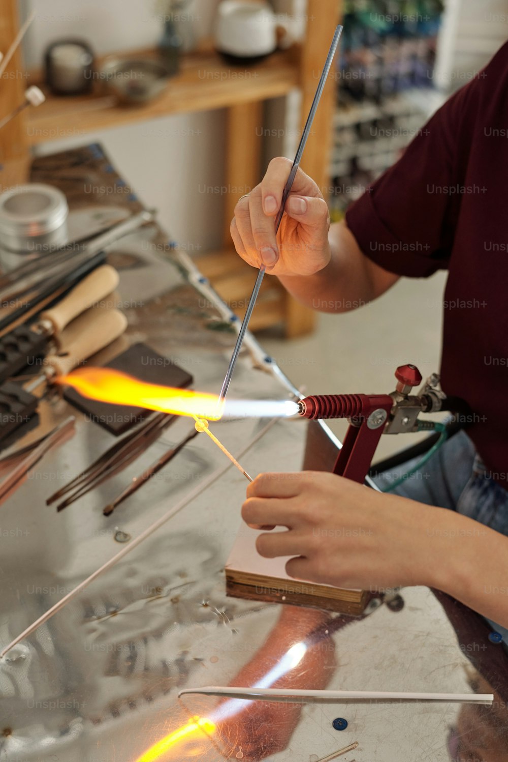 Manos de artesana contemporánea sentada junto al lugar de trabajo y quemando la pieza de trabajo en forma de palo con fuego mientras la sostiene sobre el quemador