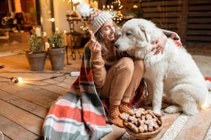 かわいい犬を連れた女性が新年を祝い、一緒に座って自宅の美しく装飾されたテラスでジンジャーブレッドを食べているポートレート