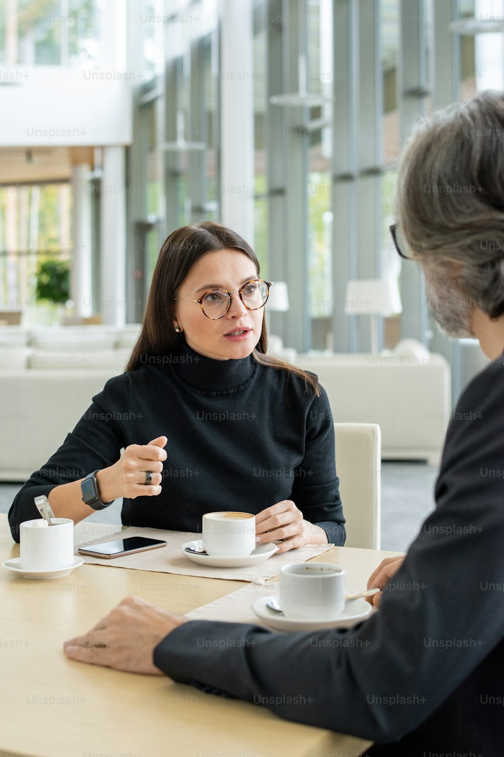 Young confident businesswoman in eyeglasses sharing her ideas of developing new business perspectives with colleague by cup of coffee