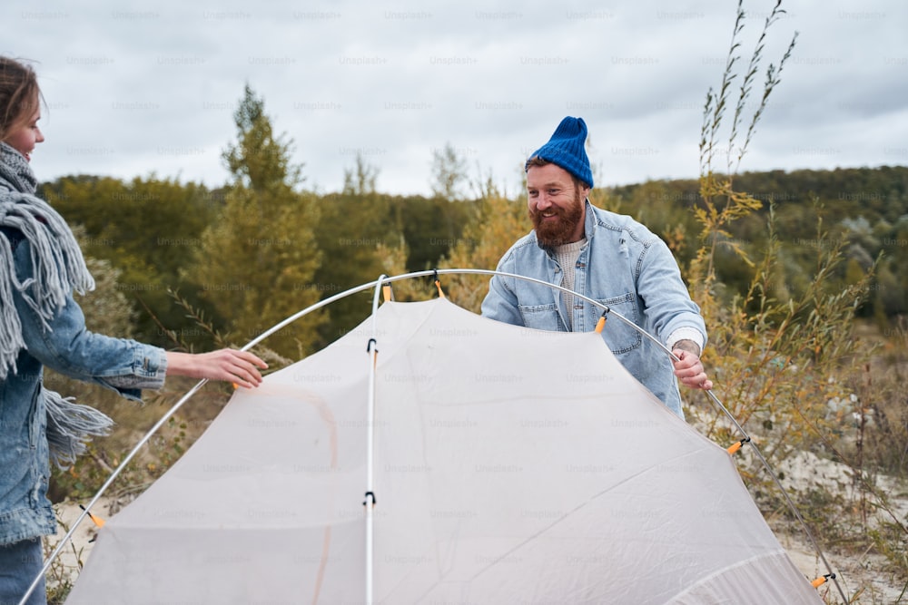 Der letzte Schliff! Zufriedener Mann baut ein Zelt auf, das er mit seiner Freundin im Wald auf offener Fläche aufgestellt hat