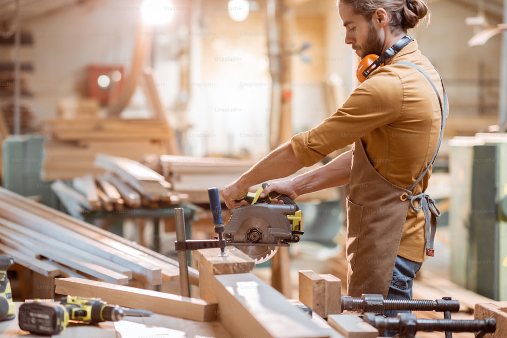 Carpintero aserrando barras de madera con sierra eléctrica inalámbrica en el taller de carpintería