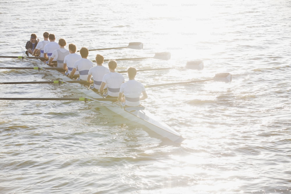 a row of rowers in white shirts row across the water