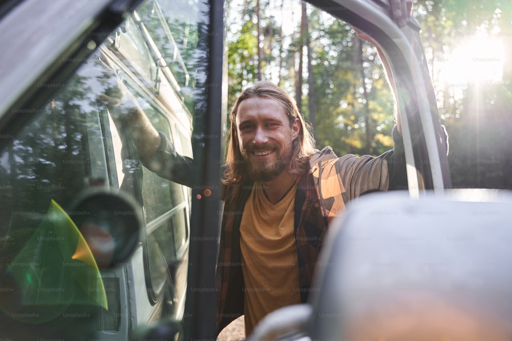 Bearded smiling man laughing while standing near the car. Active weekends, traveling, spending time at the nature concept